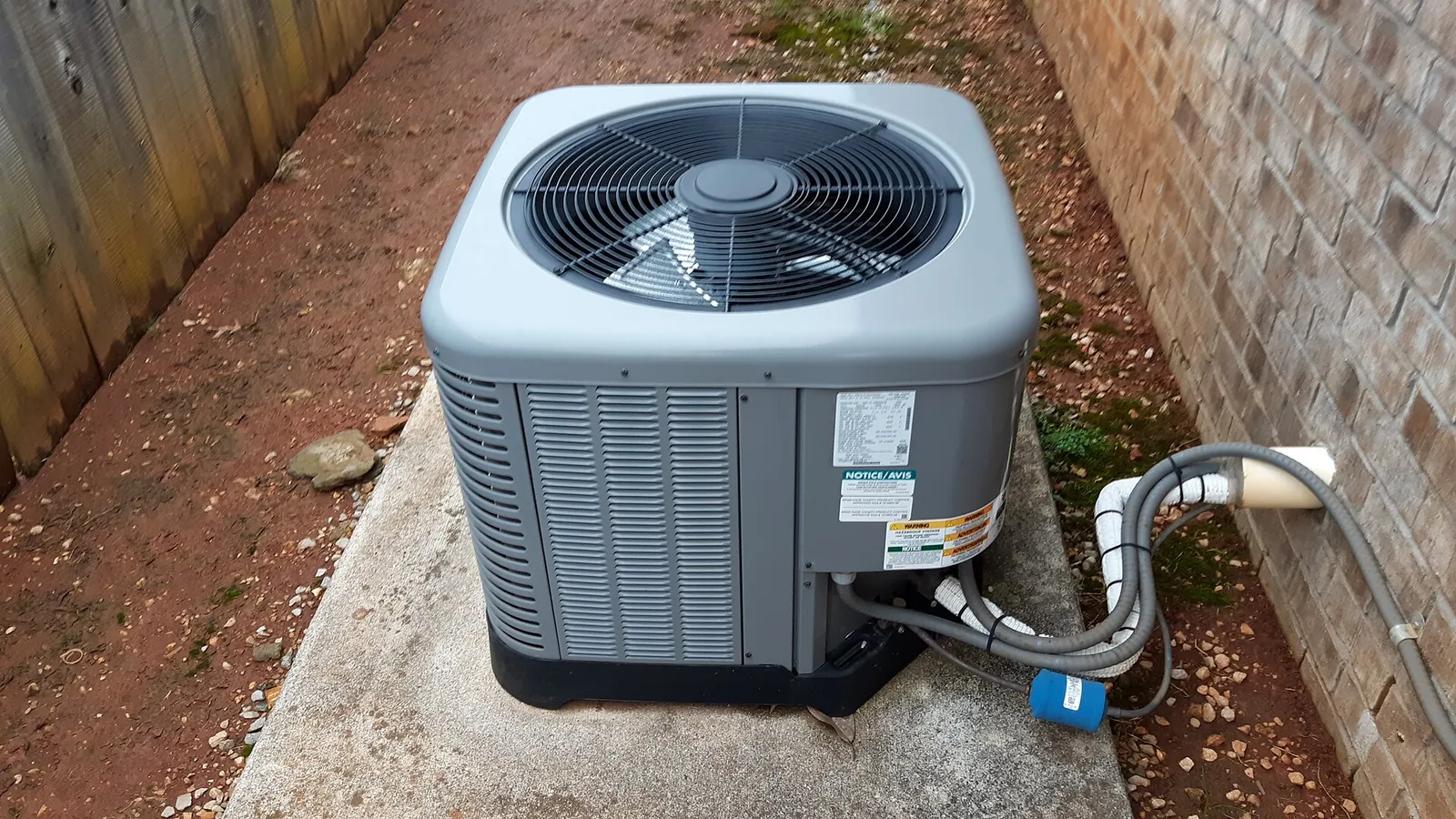 Outdoor air conditioner condenser on a concrete pad with its refrigerant line set running into a brick wall