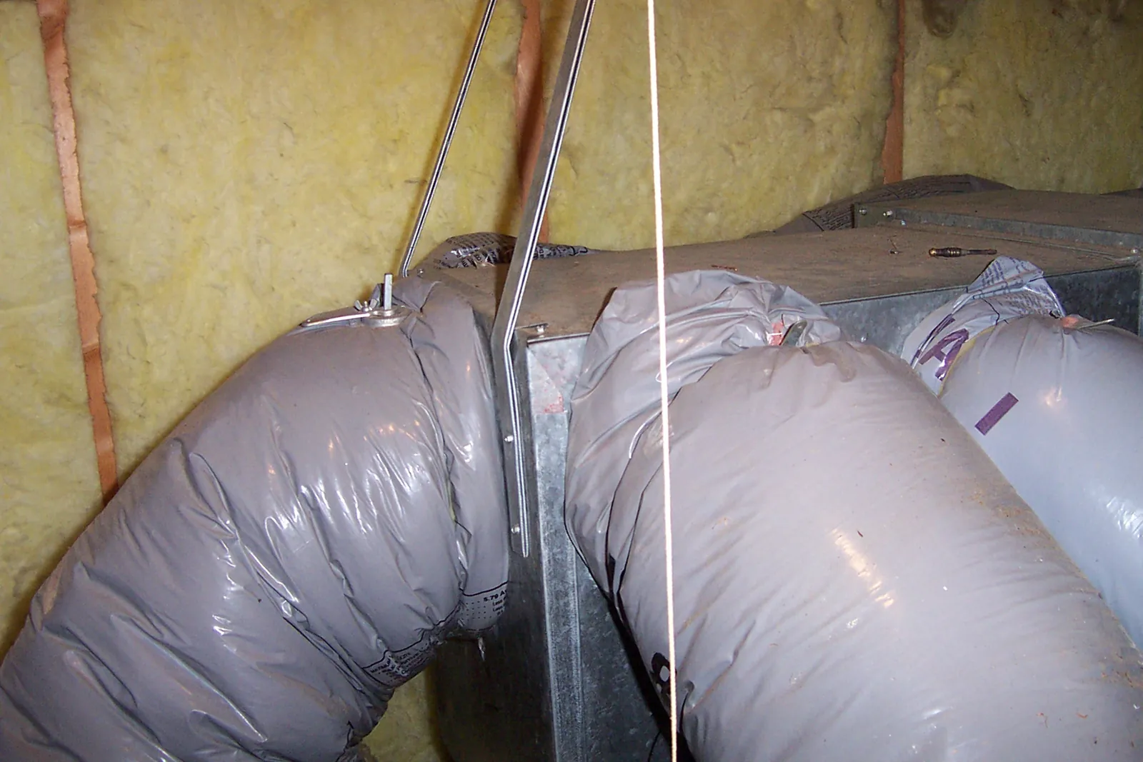 Insulated flexible ducts running off a supply plenum between fiberglass batts in an attic