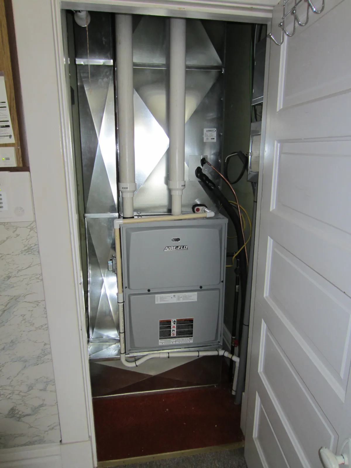 Upflow furnace and air handler in a hallway closet with PVC flue pipes and a sheet-metal supply plenum