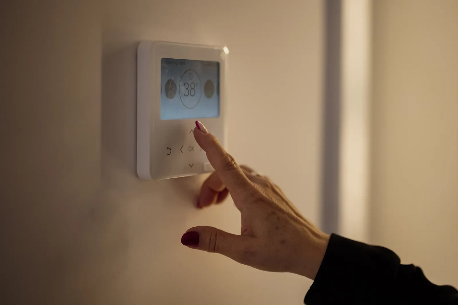 Hand pressing the buttons on a white digital wall thermostat