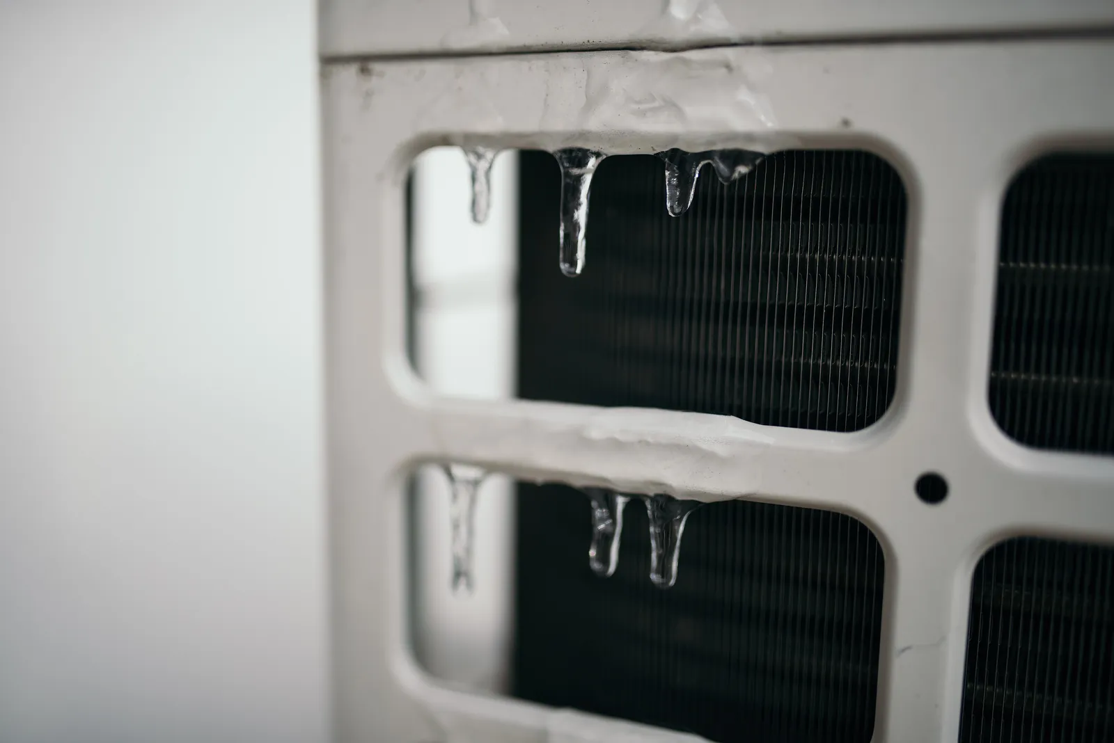 Ice hanging from the coil guard of an outdoor heat pump unit, with the frozen coil fins behind the grille