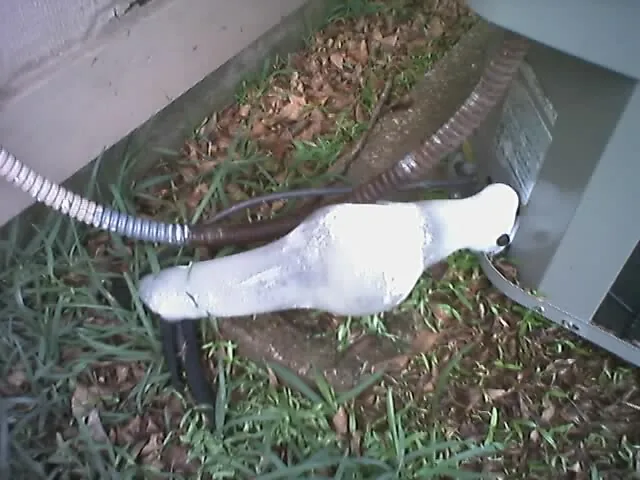 Copper suction line coated in ice where it enters an outdoor AC unit, a sign of a frozen coil